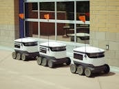 Three autonomous delivery robots parked outside a building, showcasing modern technology.